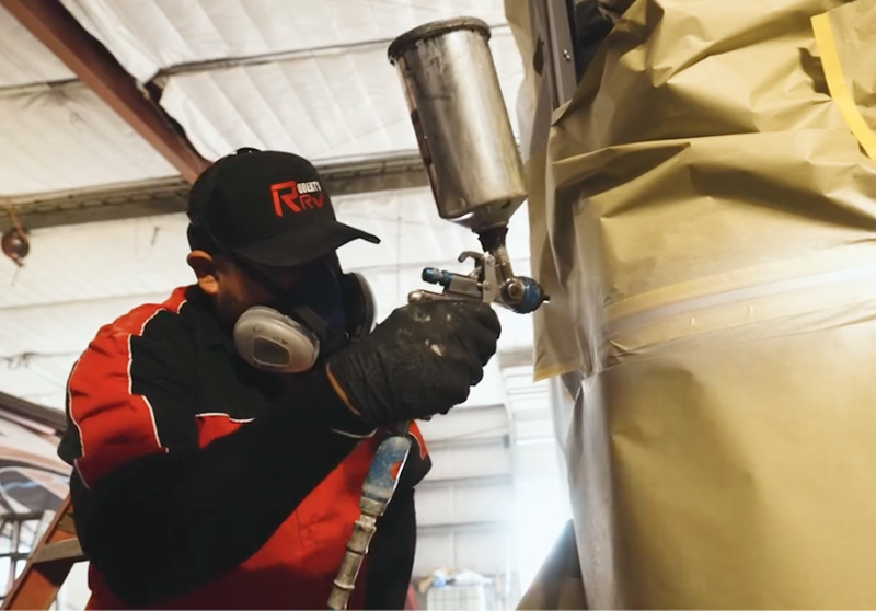 Painter in a respirator spraying custom paint on an RV